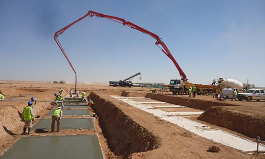A large equipment is pouring concrete to the ground with concrete pump hose.