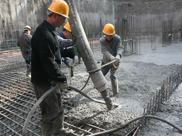 Several workers are pouring concrete to the ground with fabric reinforced concrete placement hose.